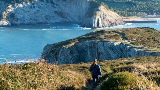 Young woman hikes in a peaceful, mountainous landscape, overlooking the serene ocean
